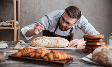 A baker carefully sprinkling flour on a loaf of bread.